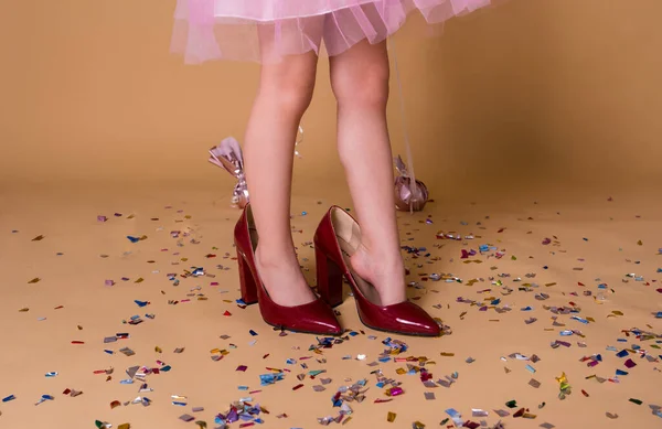 Kırmızı annenin ayakkabıları içinde bej bir arka planda duran bir çocuğun yakın plan resmi. Konfetili şenlik arka planı
