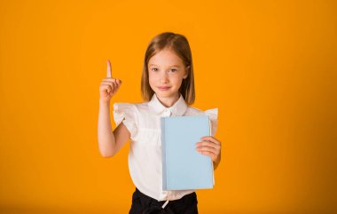 Beyaz bluzlu kız mavi bir not defteri tutuyor ve sarı arkaplanı işaret ediyor.