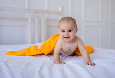 Mavi gözlü bebek bebek bezi ve turuncu havlu, odadaki beyaz pamuklu battaniyenin üzerinde sürünüyor.
