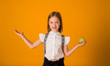 Üniformalı ve sırt çantalı zeki bir öğrenci sarı arka planda bir elma tutuyor..