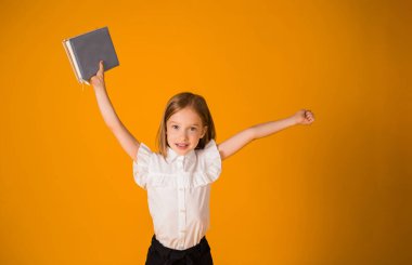 Üniformalı neşeli bir kız, sarı arka planda mavi bir not defteriyle mekanın bir kopyasıyla duruyor. Okula geri dön.