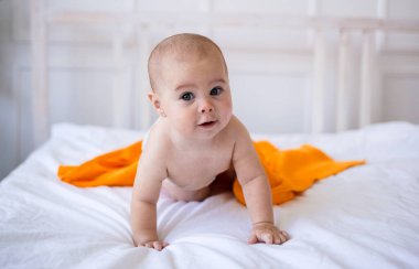 Bebek bezli ve turuncu havlusu olan bir kız yatakta emekliyor. Çocuk gelişimi