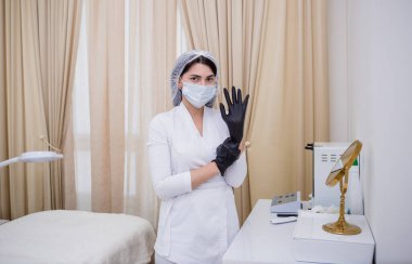 Beyaz üniformalı bir kozmetikçi ofiste siyah tek kullanımlık eldiven takıyor.