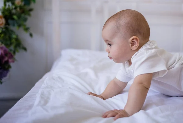 portrait of a baby girl in a white bodysuit crawling on the bed