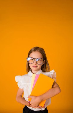 a schoolgirl in a uniform and glasses holds textbooks on a yellow background with a place for text. Back to school