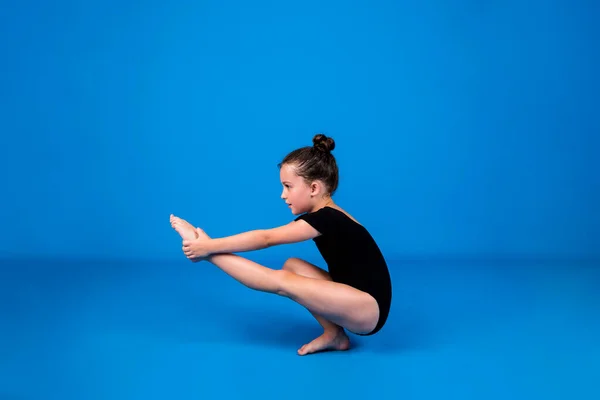 Eine Fokussierte Kleine Turnerin Führt Eine Gleichgewichtsübung Auf Blauem Hintergrund — Stockfoto