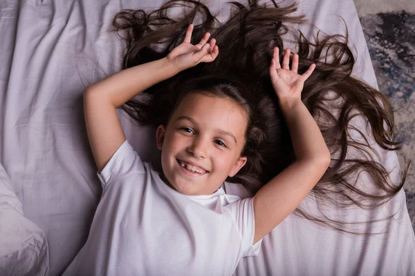 Egy Kis Barna Lány Pizsamában Fekszik Szürke Ágyneműn Ágyon — Stock Fotó