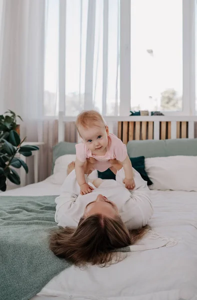 ママはベッドに横になって赤ん坊の女の子を持ち上げてる — ストック写真