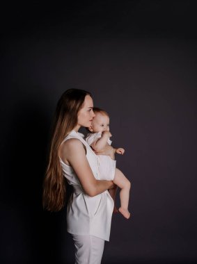 Beyaz takım elbiseli bir anne siyah bir arka planda kucağında bir kız çocuğunu tutuyor.