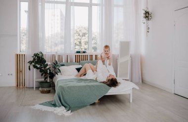 Anne yatakta uzanıyor ve kızını kucağına alıyor.