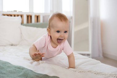 Pembe elbiseli mutlu bir kız bebek pamuklu çarşafların üzerinde sürünüyor odadaki yatakta.