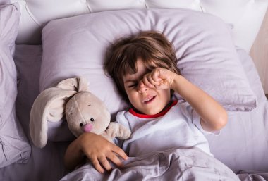 Pijamalı küçük bir çocuk oyuncak dolu bir yatakta uyanıyor.