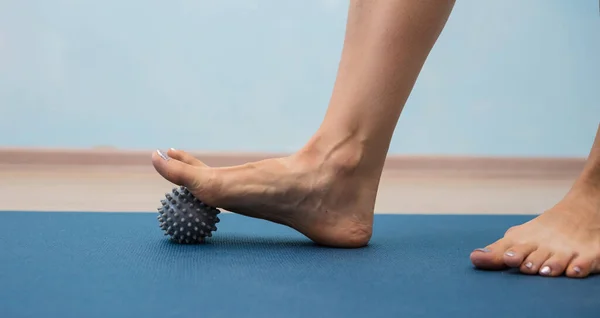 Mavi arka planda gri bir masaj topunu yuvarlayan bacakların yakın plan görüntüsü.
