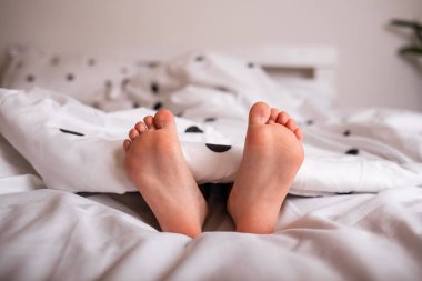 Yatağın üzerindeki battaniyenin altından bir çocuğun bacaklarının yakın çekimi.