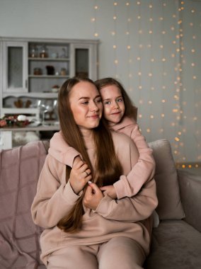 Sweatshirt giymiş küçük bir kız kanepede oturmuş annesine sarılıyor.