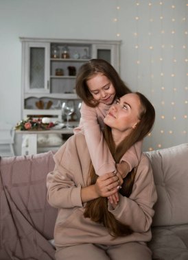 Güzel bir anne ve küçük bir kız kanepede oturmuş birbirlerine sarılıyorlar.