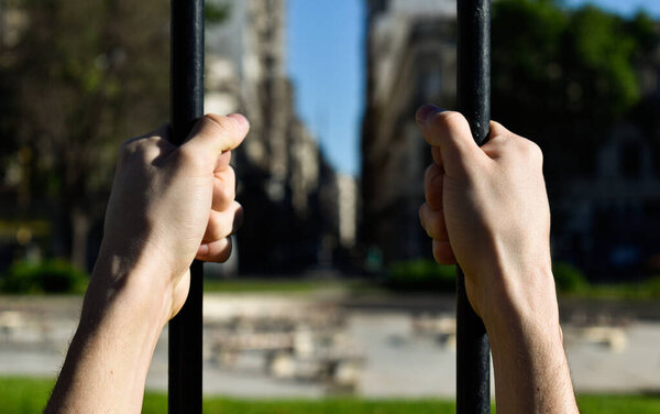 hands holding a fence with city view