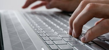 Adamın elleri modern bir bilgisayarda yazıyor. Tamamen gri, arka planı olmayan bir fotoğraf.