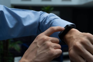 Akıllı bir dokunmatik saatle etkileşim halinde olan bir adama yaklaş. Akıllı telefonuna bağlanan saate dikkat et. Yaşam tarzı. Tanınabilir insanlar yok.