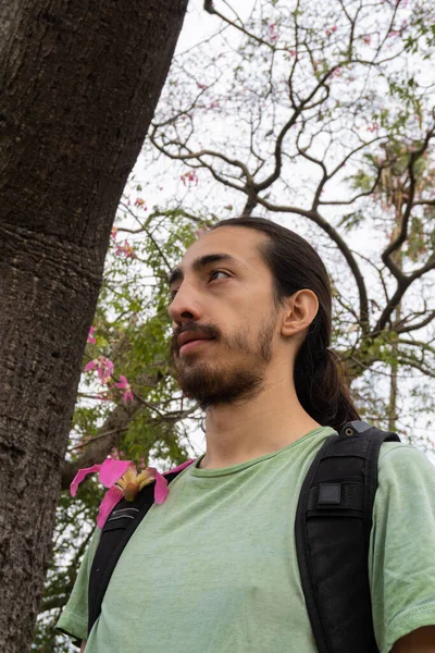 vertical photo of a man looking at the horizon with his explorer backpack, standing in the middle of the forest.