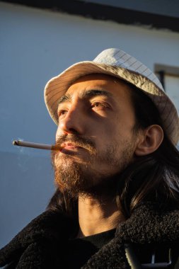 Sigara içen ve ufka alçak açılı fotoğrafla bakan bir adamın yakın çekimi. Modaya uygun bir adam. Genç asi. 31 Mayıs veya Dünya Sigara Karşıtı Günü.