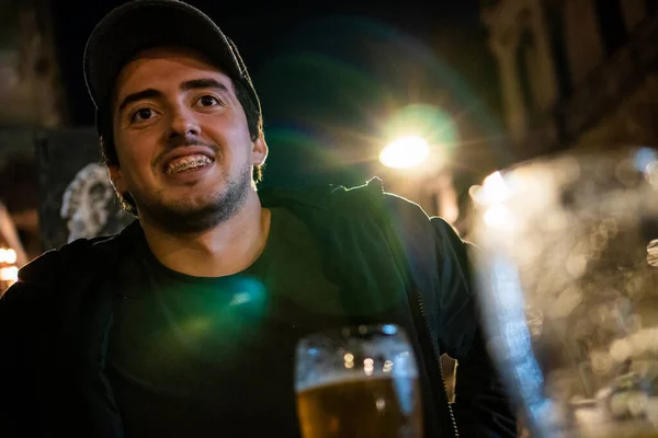 man laughing while drinking a beer in an open-air bar