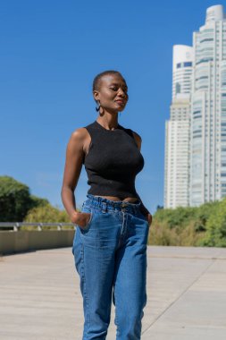 Siyahi bir Afro-Amerikalı kadın bir şehir parkında kameraya bakıyor..