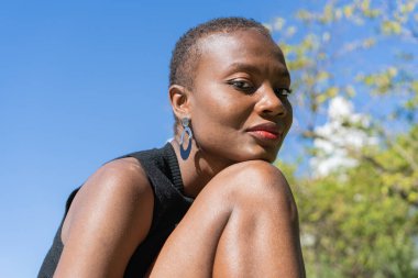 Siyahi bir Afro-Amerikalı kadın, kafası dizlerinin üzerinde dinleniyor ve bir süre sonra kameraya bakıyor..