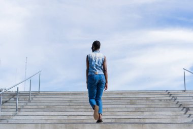 Siyah Afrikalı kadın merdivenleri tırmanıyor, gökyüzü geçmişi var.
