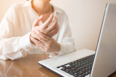 Ofis sendromu. İş yerinde dizüstü bilgisayar kullanan genç bir kadın el ağrısı çekiyor. Karpal tünel sendromu veya tetik parmağı için mesleki risk faktörü. Sağlık ve tıbbi konsept.