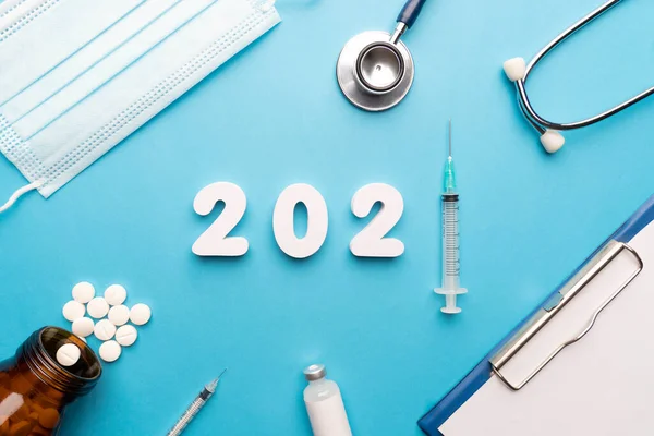 2021 Happy New Year banner for health care and medical concept. 2021 number with syringe, stethoscope, sugical face mask, doctor order chart, pills bottle and medicine vial on blue background.