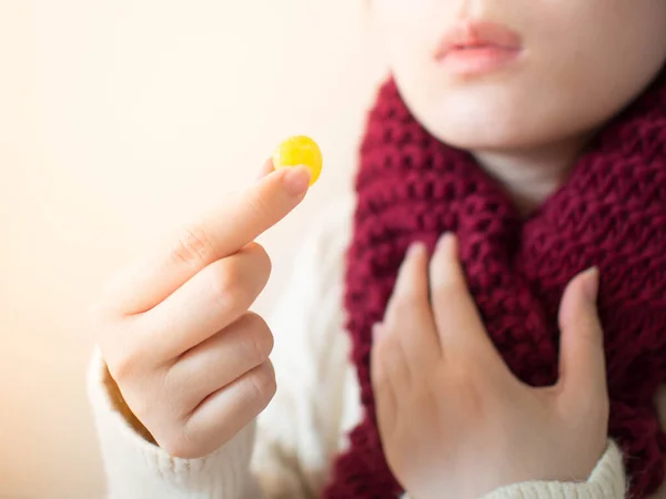 Boğaz ağrısı, sinir bozucu öksürük ve ağız ağrısı için ballı limon aromalı pastil alan bir kadın. Kışın eşarplı, hasta ve üşümüş bir kızın yakın çekimi. Sağlık hizmeti kavramı.