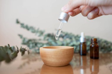 Kadının eli pipeti tutuyor ve okaliptüs yağı damlatıyor doğal okaliptüs yapraklı bir kaba, ahşap bir masa üzerinde. Aromaterapi, spa, cilt bakımı veya bitkisel tıp konsepti.