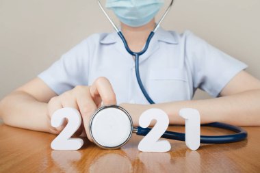 2021 Tıbbi ve Sağlık Hizmetleri konsepti için mutlu yıllar. Doktor yüz maskesi takıyor ve doktor masasında 2021 numaralı steteskopu tutuyor..