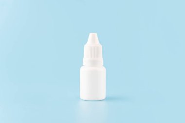 Açık mavi arka planda göz damlası ya da kulak damlası şişesi. Sıvı için boş beyaz plastik kap. İlaç ambalaj ürünleri..