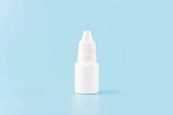 Eye drop or ear drop bottle on light blue background. Blank white plastic container for fluid. Pharmaceutical packaging product.