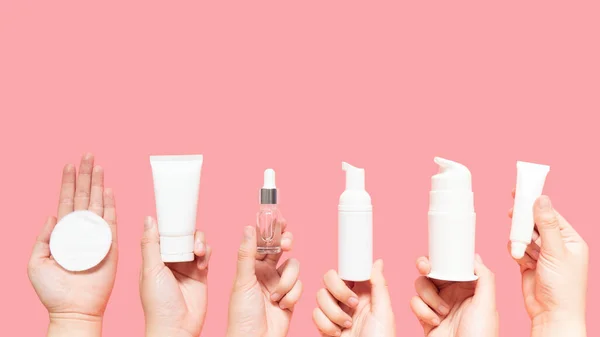 Cilt bakımı sağlıklı cilt için rutin bir adımdır - kadın elleri yüz pamuğu pedi, köpük, temel yağ, serum, losyon ve pembe arka planda göz kremi paketleri. Güzellik ve kozmetik konsepti. Boşluğu kopyala.