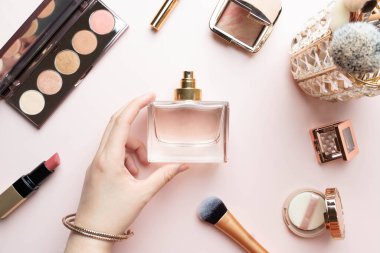 Pembe makyaj sehpasında makyaj malzemesi olan parfüm şişesini tutan kadın. Kokulu kozmetik güzellik ürünü. Güzellik blogcusu kavramı. Düz yatıyordu.