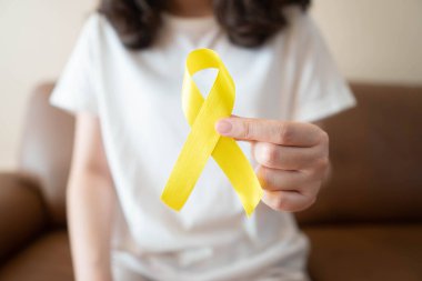 Endometriyozis, intihar önleme, sarkoma kemiği kanseri, mesane kanseri, karaciğer kanseri ve çocukluk kanseri konsepti için sarı altın kurdele farkındalığı sembolü taşıyan genç bir kadın. Sağlık hizmetleri.