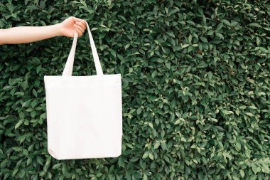 Boş beyaz çanta bez kumaş ve kabzası da tasarım. Çevreci kadınların el ele tutuşması ya da yeşil yapraklar üzerinde tekrar kullanılabilen alışveriş torbaları. Plastik poşet ve ekoloji konsepti yok. Boşluğu kopyala.