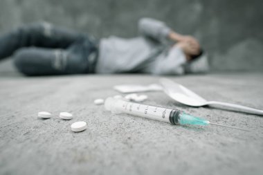 Uyuşturucu bağımlılığı ve zihinsel yoksunluk semptomları. Depresyondaki kadın şırıngayla beton zeminde yatıyor, uyuşturucu kullandıktan sonra pişirilmiş eroin kaşığı ve haplar. Uyuşturucu Bağımlılığına Karşı Uluslararası Gün.