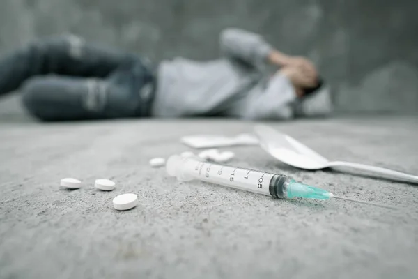 Uyuşturucu bağımlılığı ve zihinsel yoksunluk semptomları. Depresyondaki kadın şırıngayla beton zeminde yatıyor, uyuşturucu kullandıktan sonra pişirilmiş eroin kaşığı ve haplar. Uyuşturucu Bağımlılığına Karşı Uluslararası Gün.