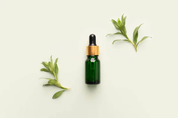 Natural herbal serum or essential oil products. Top view of green glass vial with dropper and fresh leaves on green background. Skincare, spa, aromatherapy and medicine concept.