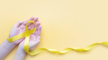 Sarı arka planda sarı altın kurdeleli farkındalık. İntihar önleme, endometriyozis, sarkoma kemik kanseri, mesane kanseri, karaciğer kanseri ve çocukluk kanseri kavramını destekleyen sembol.