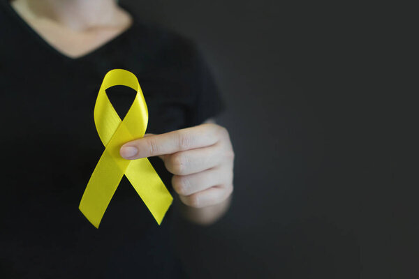 Всемирный день предотвращения самоубийств. Человеческие руки держат в руках символ осознания желтой ленты для предотвращения самоубийства на черном фоне. Концепция психического здоровья.