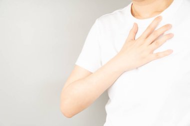 Gri arka planda göğüs ağrısı çeken genç bir kadın. Göğüs ağrısı anjini, kalp krizi, GERD ya da kostokondritin nedenleri. Sağlık ve kardiyolojik konsept. Kapat..