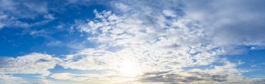 Mavi gökyüzündeki kabarık beyaz bulutların ardında parlak güneş ve manzara arkaplanı görüntüsü