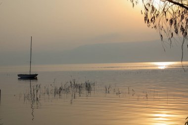 Gölün üzerinde gün doğumu. Gün batımında sakin sularda yüzen bir tekne..
