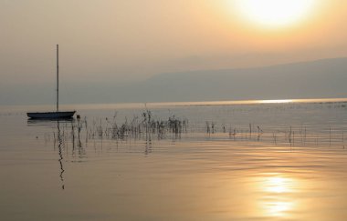 Gölün üzerinde gün doğumu. Gün batımında sakin sularda yüzen bir tekne..