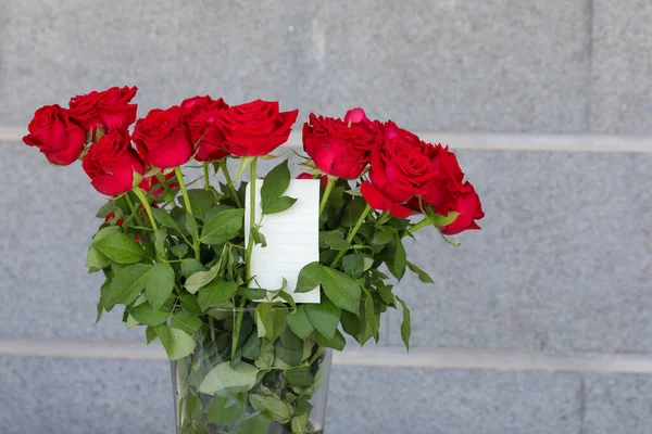 花瓶里有一束红玫瑰，还有一张写问候语的白纸. — 图库照片